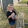 child, girl, smile, blonde_hair, black_shirt, denim_shorts, sneakers, outdoor, tree, bench, grass, sidewalk, bottle, daylight, people, park, casual_clothing, happy, person, nature
