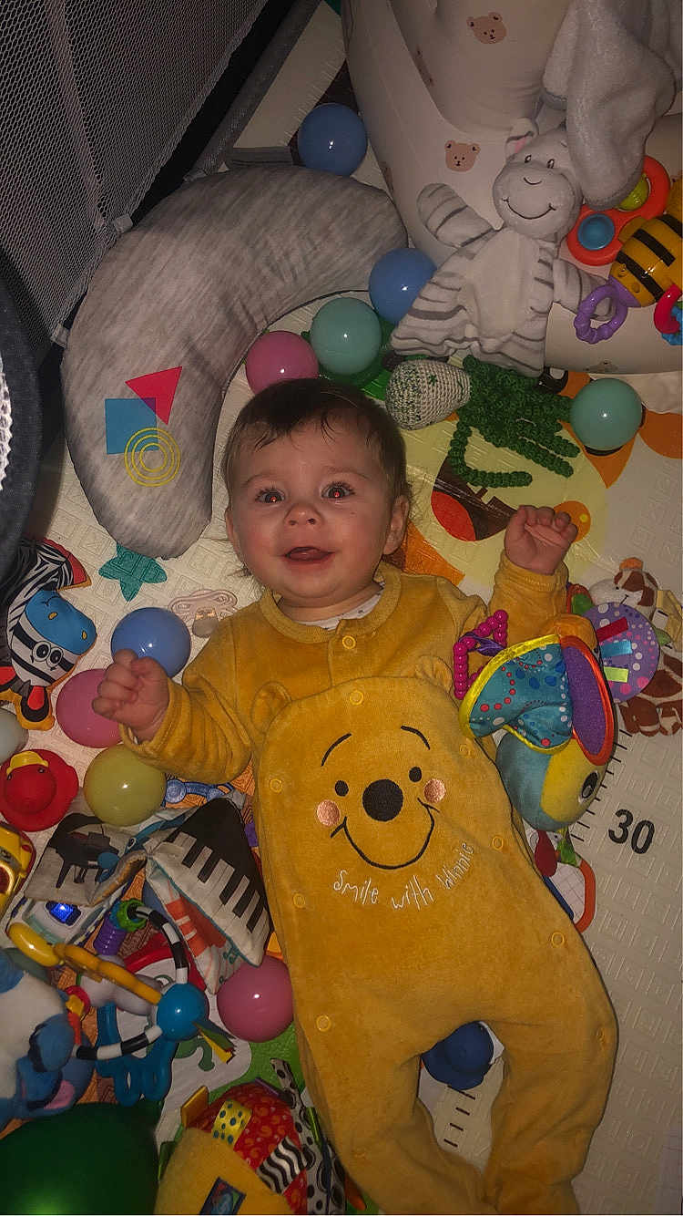 Kayden a rejoint le concours — aidez-le/la à gagner de superbes lots ! baby, child, onesie, yellow_clothing, toys, balls, red_eye, smile, lying_down, stuffed_animal, playmat, colorful, indoor, happy, infant, soft_toys, baby_toys, baby_girl, baby_boy, cute
