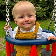 Sebastian joined the competition — help win amazing prizes! baby, chains, child, cute, daylight, face, fun, grass, greenery, happy, infant, nature, outdoor, playground, portrait, seat, smile, swing, white_shirt, yellow_overalls