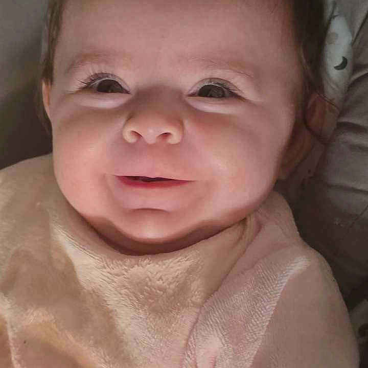 Romy participe au concours pour gagner de l'argent avec cette photo : baby, smiling, infant, close_up, face, pink_clothing, pacifier_clip, cushion, indoor, cute, child, portrait, soft_lighting, happy, young, person, cozy, warm, expression, newborn