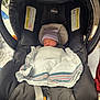 newborn, baby, car_seat, chicco, blanket, hat, sleeping, infant, child, resting, indoor, soft_lighting, tender, swaddled, comfortable, black, fabric, safety_belt, cute, peaceful