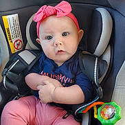 Avalynn is registered to the contest to win money with this photo: baby, blue_shirt, car, car_seat, child, child_seat, clothing, cute, expression, face, hands, headband, indoor, infant, pink_bow, pink_pants, portrait, safety, seatbelt, toy