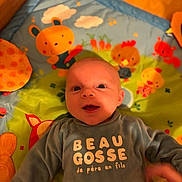 Elio participe au concours pour gagner de l'argent avec cette photo : baby, infant, play_mat, colorful, smiling, clothing, shirt, animal_illustrations, hand, indoors, floor, wooden_floor, cute, child, person, portrait, lying_down, happy, playful, expression