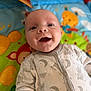 baby, infant, smile, happy, face, onesie, clothing, playmat, colorful, animal_print, cute, child, indoors, portrait, young, expression, joyful, head, lying_down, soft_focus