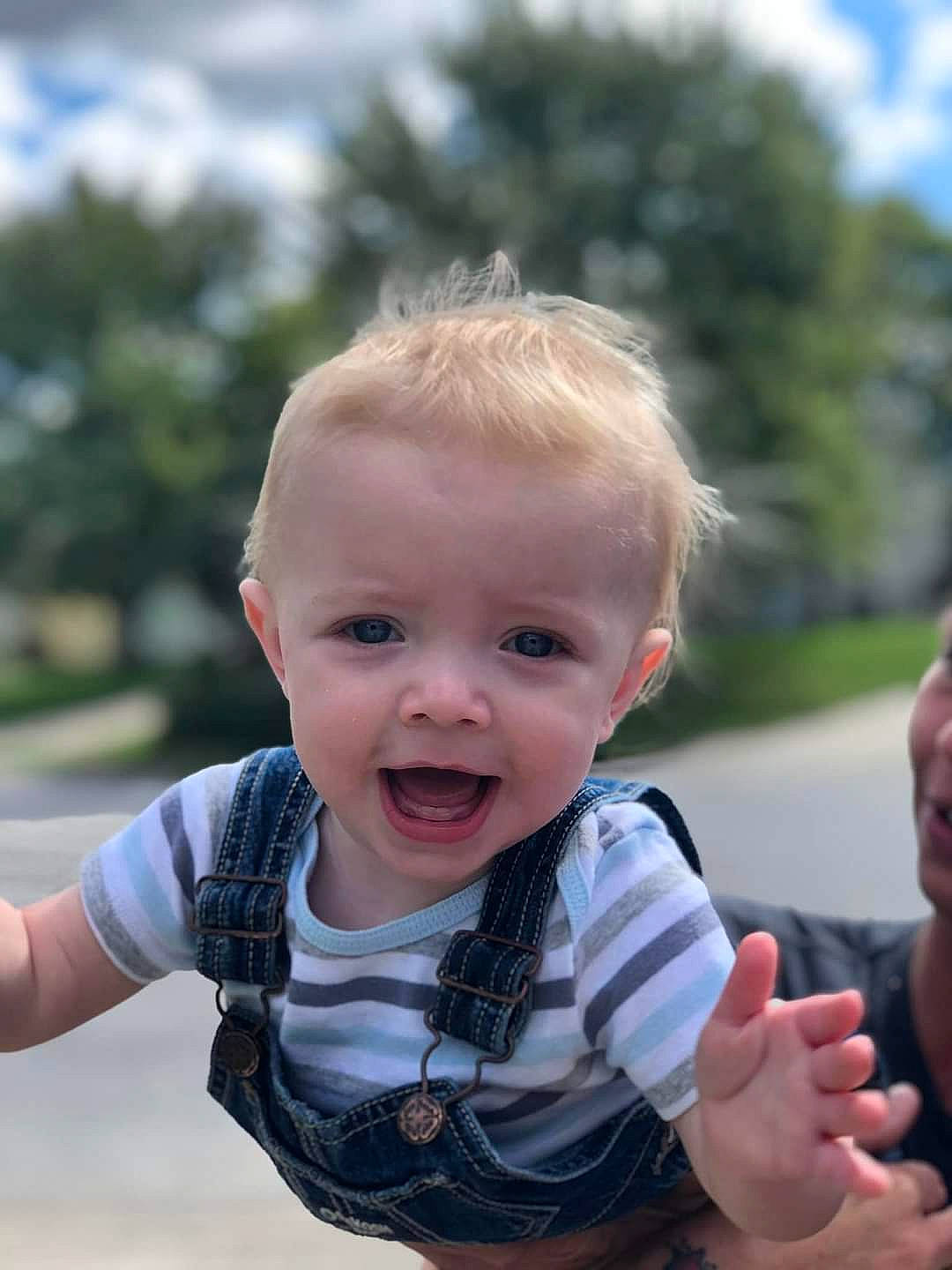 Kash is registered to the contest to win money with this photo: arm, baby, baby_toddler_clothing, cheek, face, facial_expression, finger, fun, gesture, grass, hairstyle, hand, happy, head, iris, joy, person, skin, sleeve, smile