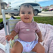 Harlow is registered to the contest to win money with this photo: baby, child, smiling, sitting, chair, outdoor, grass, quilt, shirt, diaper, person, face, happy, skin, head, suburban, car, sky, cloud, residential
