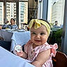 baby, child, smile, headband, pink_dress, high_chair, pacifier, indoor, restaurant, table, window, cityscape, people, woman, glass, food, furniture, happy, portrait, cute