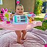 Harlow is registered to the contest to win money with this photo: baby, child, pink, activity_center, smiling, outdoor, blanket, grass, toys, happy, person, face, playtime, quilted_blanket, home, greenery, sunlight, legs, feet, cute