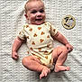 baby, infant, smiling, onesie, patterned_clothing, leopard_print, lying_down, blanket, textured_blanket, wooden_sign, age_marker, cute, child, happy, skin, foot, hand, head, face, blue_eyes