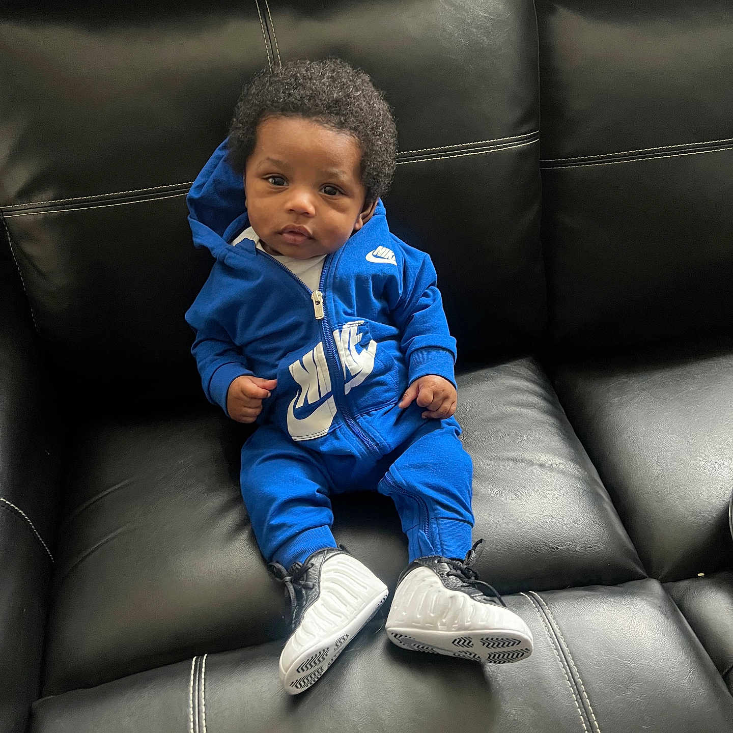 Noah joined the competition — help win amazing prizes! baby, black_leather_couch, blue_clothing, casual, child, comfortable, curly_hair, cute, expression, fashion, footwear, indoor, infant, nike, person, portrait, seated, sneakers, tracksuit, young_child