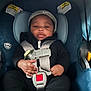 baby, car_seat, child, infant, seatbelt, clothing, cap, black_outfit, hand, face, safety, indoor, cute, young_child, person, headwear, seat, straps, footwear, expression