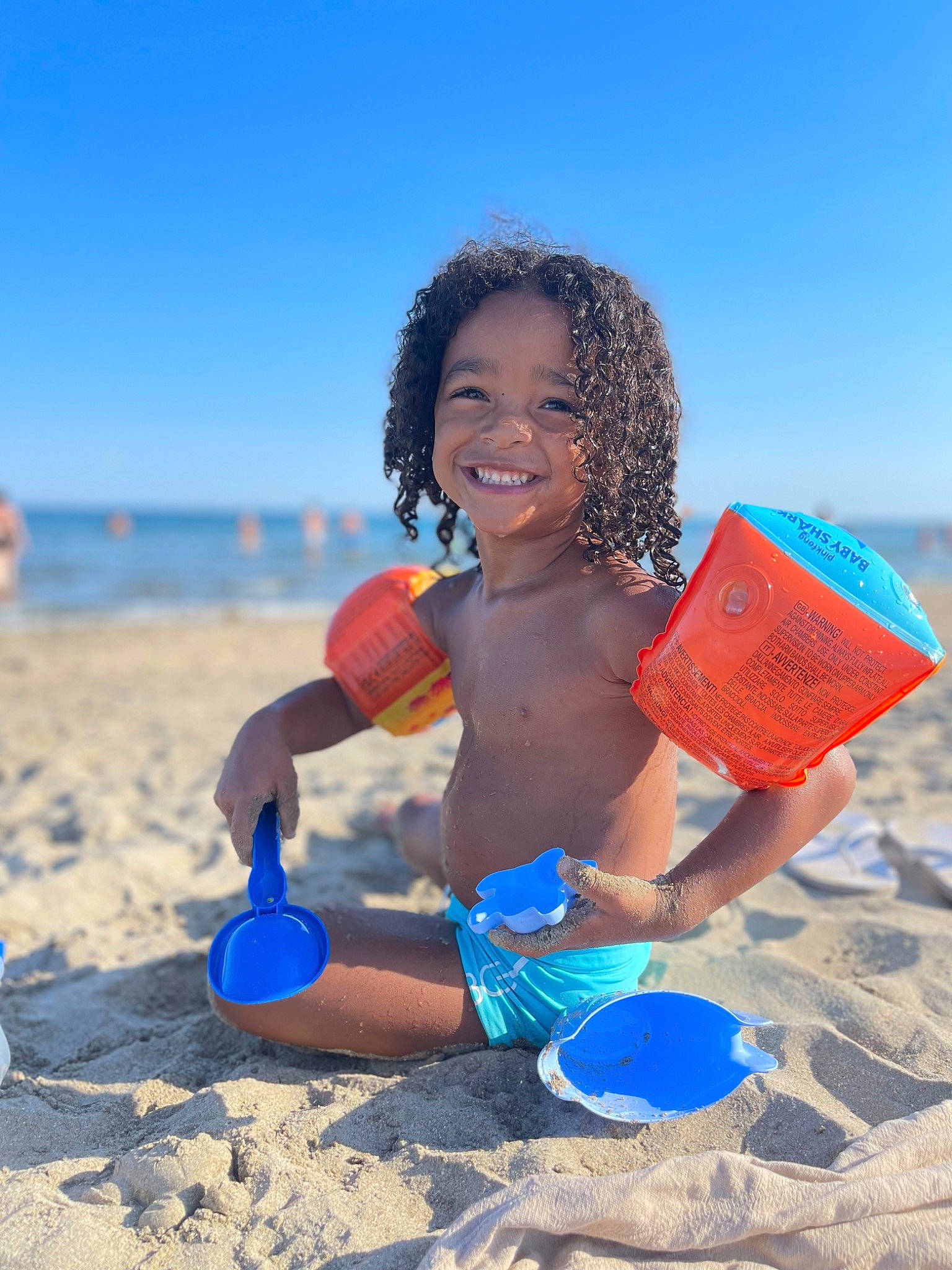 Marlonn a rejoint le concours — aidez-le/la à gagner de superbes lots ! azure, ball, beach, fun, happy, joy, leisure, people_in_nature, people_on_beach, person, personal_protective_equipment, recreation, sand, shore, shorts, sky, smile, summer, swimwear, toddler