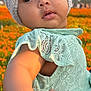 baby, child, knitted_hat, flower, bracelet, hand, dress, lace, outdoor, field, flowers, nature, person, skin, face, cute, infant, holding, sunlight, expression