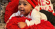 Amir joined the competition — help win amazing prizes! baby, red_hat, red_cushion, valentines_day, balloon, smiling, happy, infant, cute, holiday, celebration, sign, love, indoor, cozy, person, clothing, face, headwear, couch