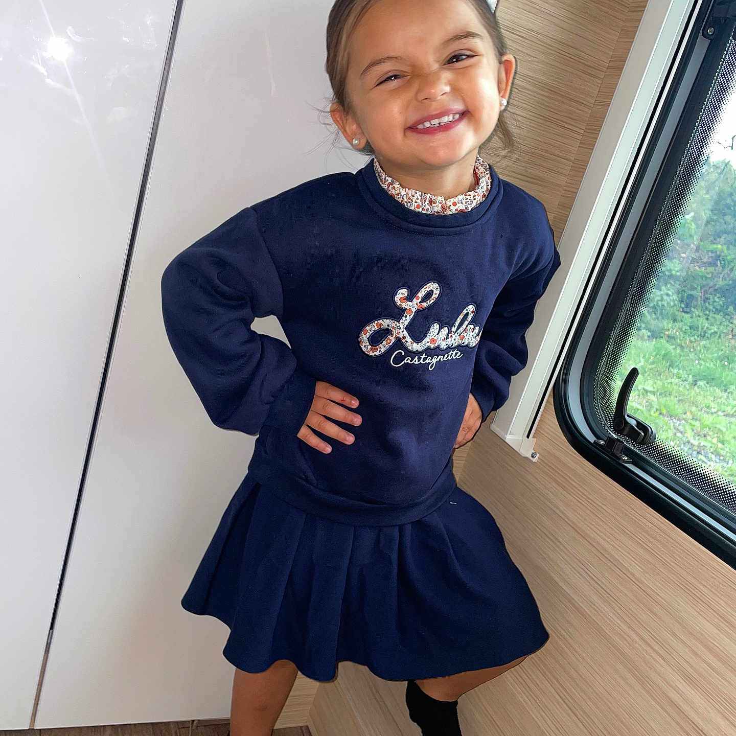 Dailly participe au concours pour gagner de l'argent avec cette photo : blue_clothing, cabinet, child, earrings, fashion, feet, floor, girl, happy, indoor, person, portrait, pose, skirt, smile, sock, sweatshirt, window, wooden_floor, young