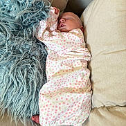 Jessica is registered to the contest to win money with this photo: baby, sleeping, infant, blanket, couch, pillow, floral_pattern, swaddle, peaceful, indoor, child, foot, hand, soft_texture, cozy, relaxation, home, comfort, rest, newborn