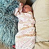 baby, sleeping, infant, blanket, couch, pillow, floral_pattern, swaddle, peaceful, indoor, child, foot, hand, soft_texture, cozy, relaxation, home, comfort, rest, newborn