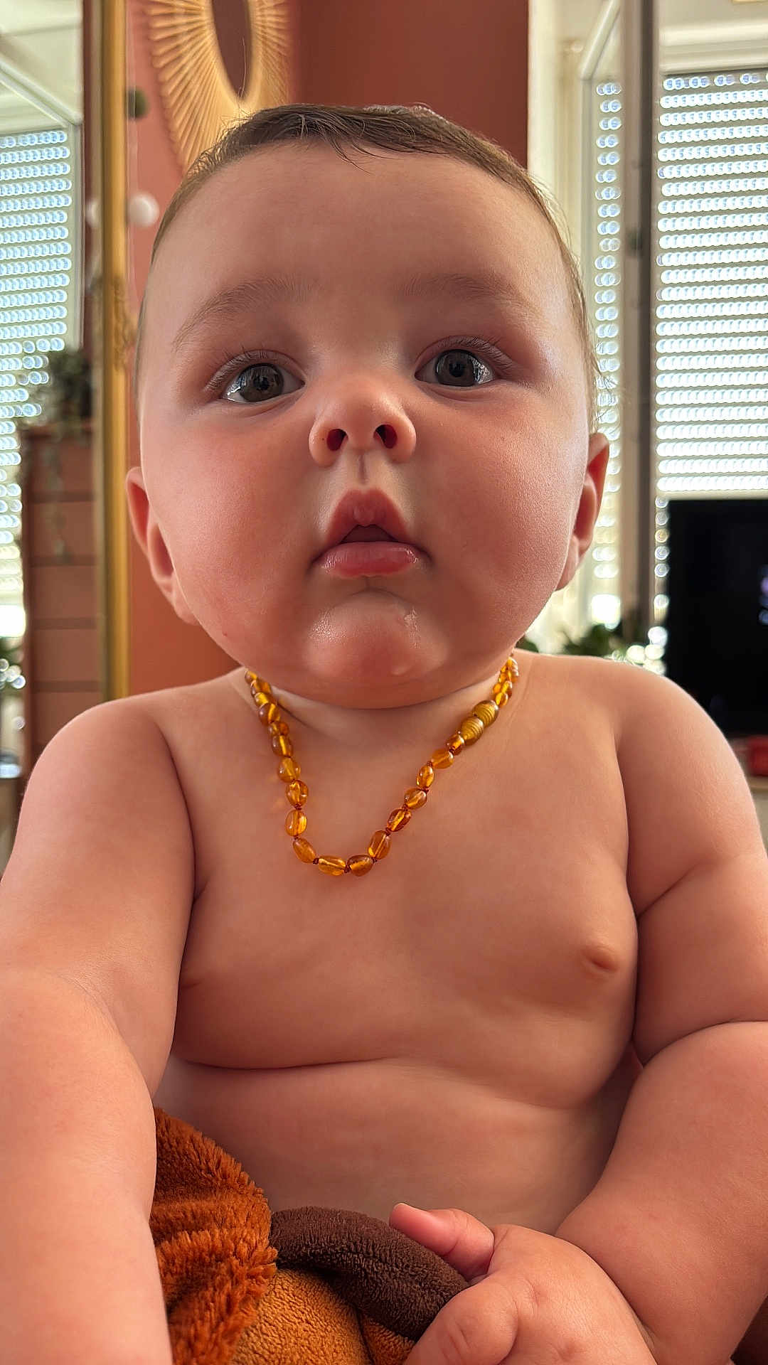 Elie participe au concours pour gagner de l'argent avec cette photo : baby, child, necklace, amber, skin, chubby, hand, blanket, indoor, window, curious, portrait, closeup, face, expression, young, furniture, room, natural_light, person