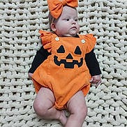 Aurora is registered to the contest to win money with this photo: baby, infant, child, halloween, pumpkin_costume, orange_outfit, bow_headband, jack_o_lantern, costume, blanket, cream_blanket, lying_down, portrait, face, indoors, cute, festive, black_sleeves, photography, closeup