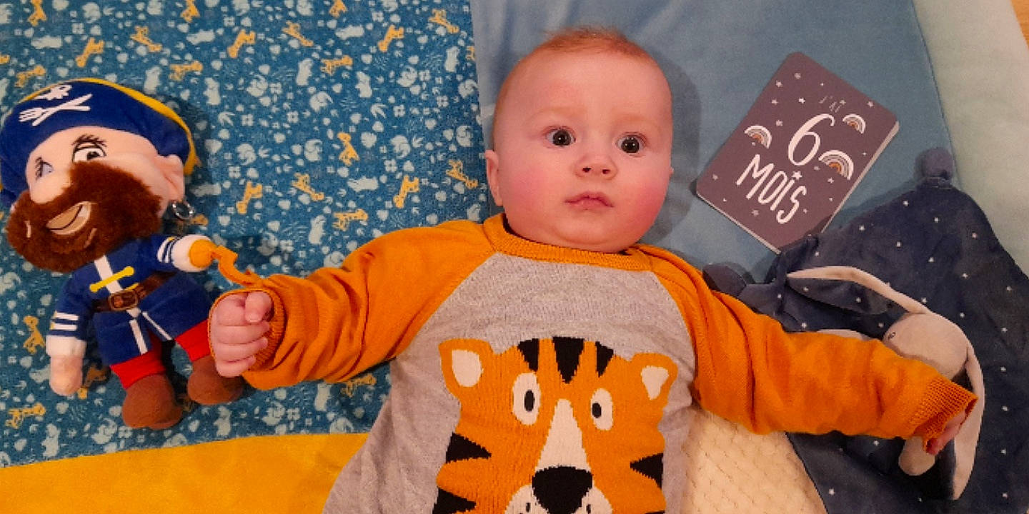 Mathéo a rejoint le concours — aidez-le/la à gagner de superbes lots ! baby, baby_products, baby_toddler_clothing, blue, cheek, child, fun, happy, linens, nose, orange, pattern, person, room, skin, sleeve, stuffed_toy, t_shirt, textile, toddler
