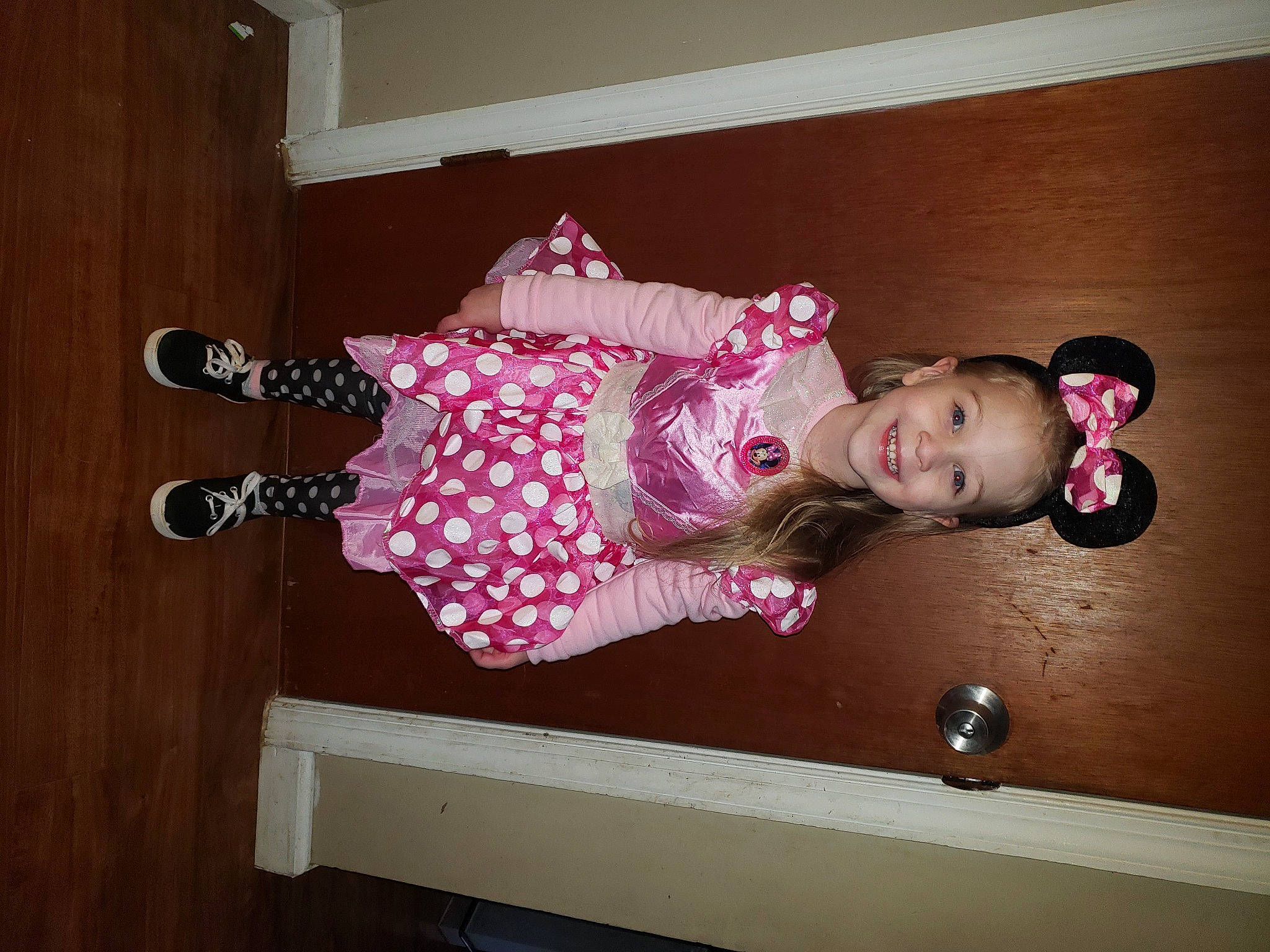 Leila is registered to the contest to win money with this photo: baby_toddler_clothing, child, dress, floor, flooring, happy, hardwood, human_leg, joy, magenta, pattern, person, pink, room, sleeve, smile, sock, standing, thigh, toddler