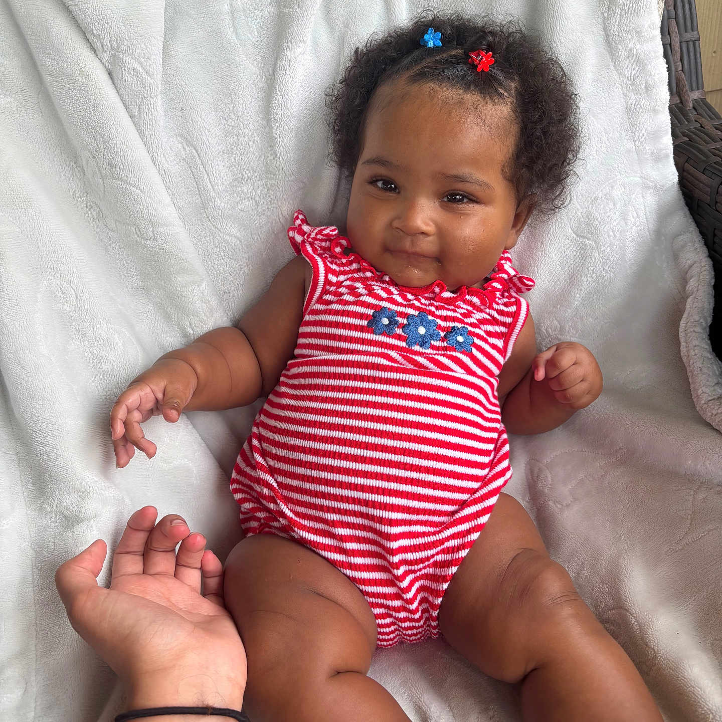 Akarii is registered to the contest to win money with this photo: baby, blanket, blue_flower_hair_clips, cheeks, child, curly_hair, cute, footwear, hand_holding, indoors, infant, legs, portrait, rattan_chair, red_striped_clothing, relaxing, skin, smile, soft_texture, white_blanket