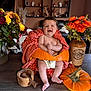 baby, pumpkin, orange_towel, flowers, vase, wooden_table, mortar_and_pestle, smiling, indoor, decor, diaper, brown_wall, shelf, horse_figurine, plant, pottery, child, happy, portrait, cozy
