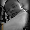 baby, sleeping, black_and_white, portrait, close_up, infant, peaceful, soft_light, striped_clothing, arm, face, cozy, newborn, person, candid, monochrome, resting, cute, tender, calm