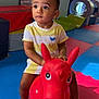 Aïjaz a rejoint le concours — aidez-le/la à gagner de superbes lots ! toddler, child, toy, red, inflatable, horse, playroom, foam_mat, indoor, curious, sitting, yellow_shirt, short_hair, barefoot, plastic_toy, colorful, play_equipment, floor, expression, young_child