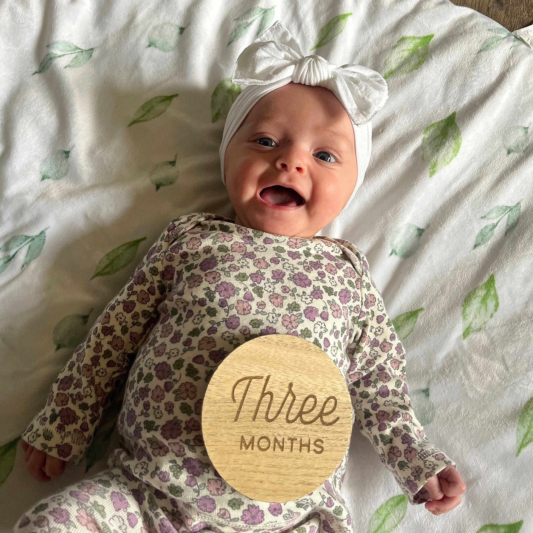 Zarriah is registered to the contest to win money with this photo: baby, blanket, bow, close_up, floral_outfit, hand, happy, headband, infant, leaf_pattern, lying_down, milestone, nursery, onesie, open_mouth, portrait, smile, soft_lighting, three_months, wooden_disc