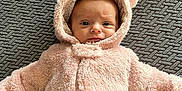 Zarriah is registered to the contest to win money with this photo: baby, infant, child, pink, furry_coat, onesie, hood, bear_ears, lying_down, textured_blanket, gray_background, cozy, cute, portrait, wide_eyes, looking_at_camera, indoor, soft_clothing, close_up, adorable