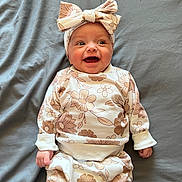 Zarriah joined the competition — help win amazing prizes! baby, blanket, bow, child, clothing, cute, expression, face, fashion, floral_pattern, hands, happy, headband, indoor, infant, laying_down, onesie, person, portrait, smile