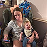 baby, child, parent, adult, smiling, sitting, lap, portrait, indoor, armchair, blanket, bib, clothing, phone, home, living_room, furniture, happy, family, photography
