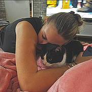 Iris a rejoint le concours — aidez-le/la à gagner de superbes lots ! person, cat, black_and_white_cat, blanket, pink_blanket, couch, indoor, snuggling, phone, television, brick_wall, casual_clothing, bracelets, hair_tie, relaxation, cozy, home, furniture, comfort, pet