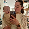 baby, baby_clothing, casual_clothing, curious, facial_expression, furniture, holding, home, indoor, jeans, knitted_sweater, mirror, natural_light, person, portrait, selfie, smartphone, sunglasses, watch, woman