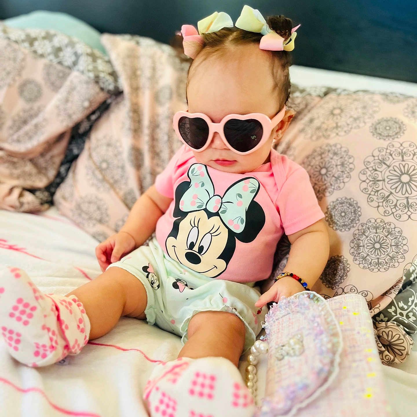 Scarlett is registered to the contest to win money with this photo: accessory, baby, bed, bracelet, child, clothing, cute, fashion, footwear, hair_bows, indoor, mickey_mouse, minnie_mouse, person, pillow, pink, portrait, purse, sunglasses, toddler