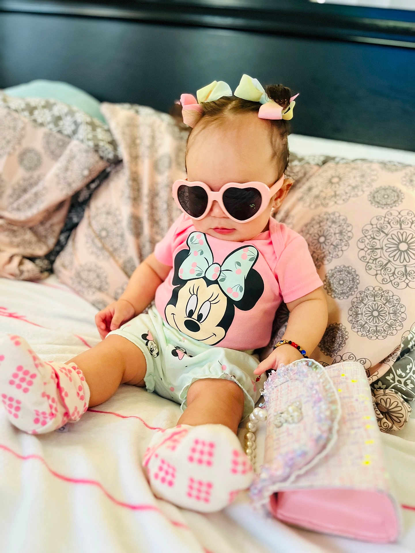 Scarlett is registered to the contest to win money with this photo: baby, child, sunglasses, pink, bed, pillow, mickey_mouse, minnie_mouse, clothing, footwear, accessory, bracelet, purse, hair_bows, cute, indoor, person, fashion, portrait, toddler