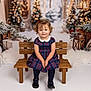 Mimi joined the competition — help win amazing prizes! toddler, child, girl, plaid_dress, wooden_bench, curly_hair, red_bow, black_shoes, christmas_tree, holiday_decor, wrapped_presents, lantern, winter_theme, snow_effect, festive, smiling, indoors, portrait, studio_photo, cozy
