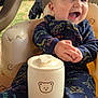 baby, child, smiling, clapping, onesie, dinosaur_pattern, seat, bear_pattern, container, outdoor, dog, black_dog, happy, infant, face, head, hands, toy, furniture, grass
