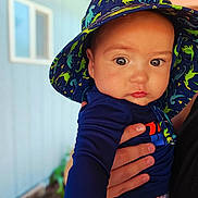 Karson is registered to the contest to win money with this photo: baby, child, hat, dinosaur_pattern, hand, blue_shirt, outdoor, portrait, cute, face, eyes, person, clothing, skin, infant, young_child, colorful, sun_hat, holding, background