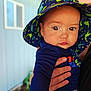 baby, child, hat, dinosaur_pattern, hand, blue_shirt, outdoor, portrait, cute, face, eyes, person, clothing, skin, infant, young_child, colorful, sun_hat, holding, background