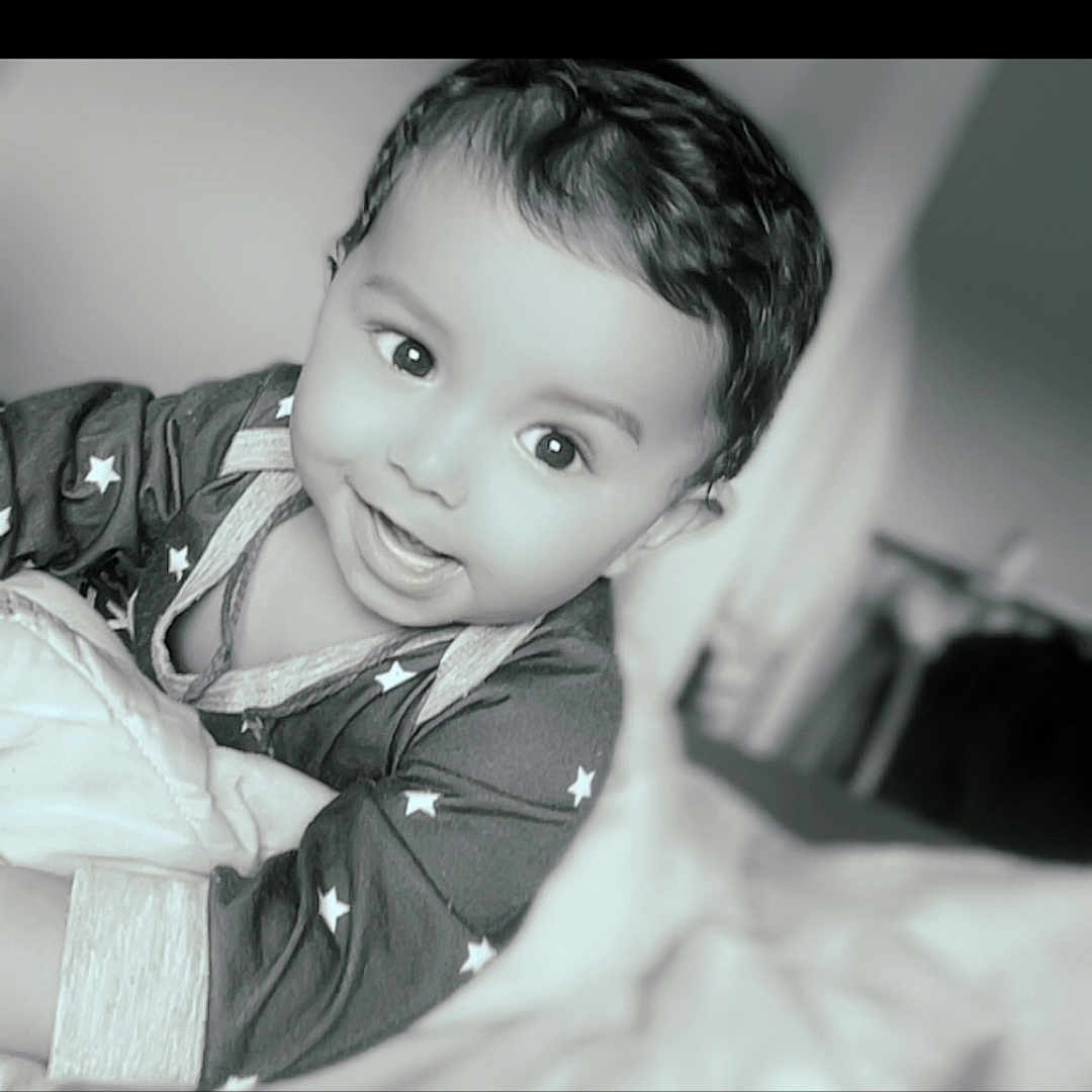 Sanji Maleappa participe au concours pour gagner de l'argent avec cette photo : baby, bed, black_and_white, blanket, child, clothing, curly_hair, cute, expression, eyes, face, happy, indoor, infant, lying_down, portrait, smiling, soft_focus, star_pattern, young_child