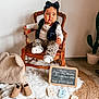 toddler, child, chair, headband, bow, leopard_print, pants, socks, wooden_chair, chalkboard, alphabet_blocks, abc, rug, blanket, baby_shoes, cactus, indoor, floor, cute, portrait