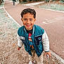 child, boy, smiling, outdoor, park, pathway, jacket, sneakers, curly_hair, casual_clothing, happy, young, person, nature, trees, fall, walking_path, standing, daylight, playful