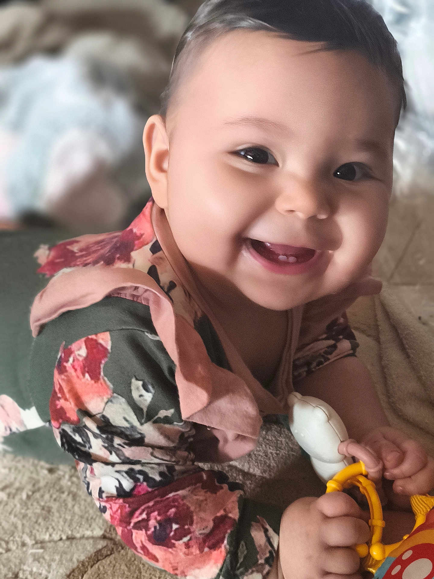 Leyna a rejoint le concours — aidez-le/la à gagner de superbes lots ! baby, smiling, toy, floral_clothing, closeup, happy, infant, hand, face, portrait, indoor, child, cute, soft_light, lying_down, young_child, skin, eyes, mouth, expression