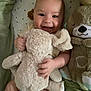 baby, smiling, stuffed_animal, plush_toy, blanket, infant, happy, cute, child, soft, cozy, indoors, sleeping_area, toddler, face, cuddly, comfort, toy, person, lying_down
