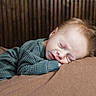 baby, sleeping, child, cozy, green_clothing, resting, soft_surface, wooden_background, peaceful, portrait, indoors, cute, infant, face, relaxing, warm_colors, closeup, young_child, comfort, serene