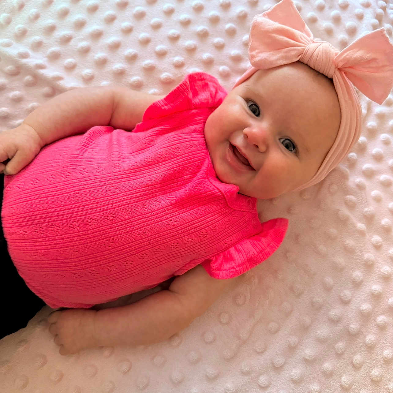 Jasmine is registered to the contest to win money with this photo: arms, baby, blanket, bow, child, comfortable, cute, eyes, face, happy, headband, indoor, infant, lying_down, pink_clothing, portrait, skin, smiling, soft, texture
