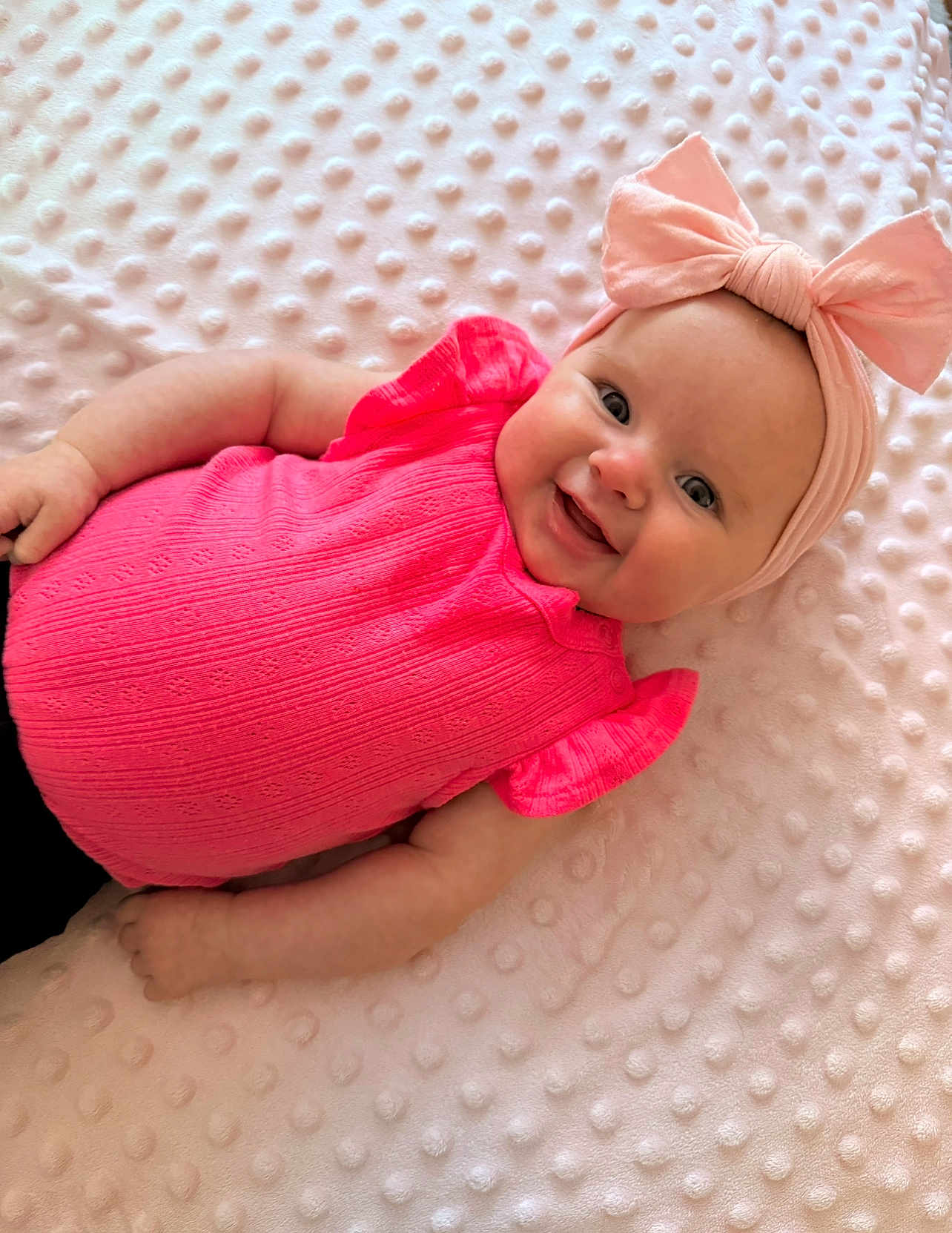 Jasmine is registered to the contest to win money with this photo: baby, infant, pink_clothing, headband, bow, smiling, happy, lying_down, blanket, texture, cute, child, portrait, soft, comfortable, indoor, skin, face, arms, eyes