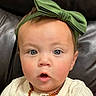 baby, child, face, headband, green_bow, blue_eyes, amber_necklace, expression, surprised, clothing, buttoned_shirt, infant, portrait, cute, indoor, leather_background, closeup, skin, person, young